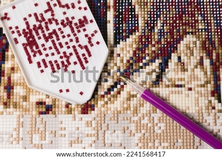 home hobby to draw a picture of rhinestones, multicolored diamond mosaic. the process of gluing a pencil of rhinestones on the canvas of the picture.