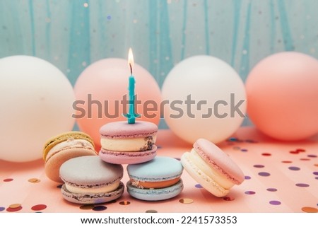 Colorful macarons and one candle on blue and pink background with decorations, happy birthday and anniversary card