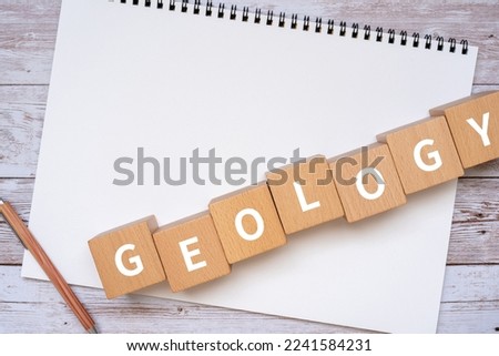 Wooden blocks with "GEOLOGY" text of concept, a pen, and a notebook.