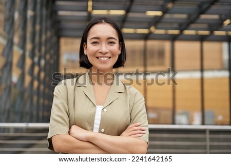People. Portrait of confident korean girl, young student cross arms on chest, standing in power pose and smiling at camera.