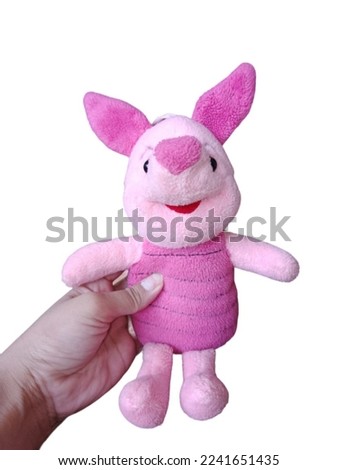 Girl's hand holding a cute pink piglet doll on a white background.
