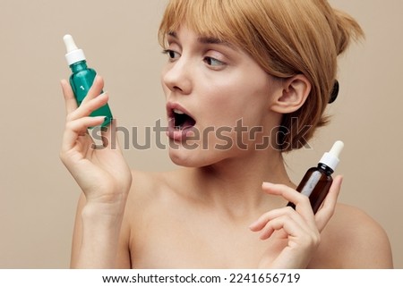 Horizontal studio shot. Close-up photo. a woman in a towel with clean smooth skin, brown hair pinned back hair on a beige background with two new face serums is surprised by a good purchase.