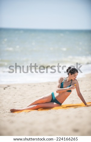 gorgeous young woman in a swimsuit on the beach applying sunscreen on her body
