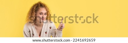 A young girl with curly hair points with a gesture on a studio background.