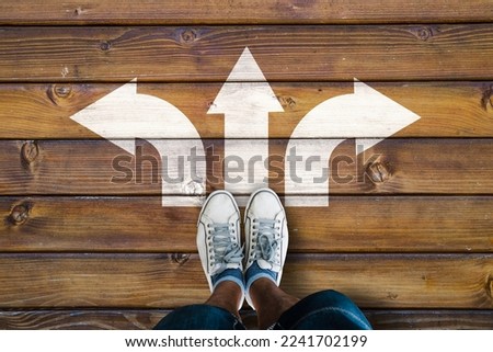 man legs in sneakers standing on wooden floor with three direction arrow choices, left, right or move forward 