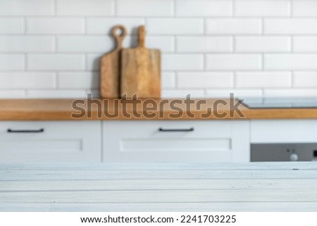 Wooden white  countertop with free space for mounting a product or layout against the background of a blurred white kitchen with cuting board. Horizontal orientation. 