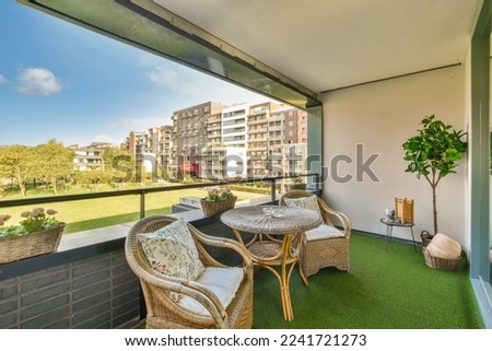 a balcony with chairs, tables and a plant on the grass area in front of the apartment's windows