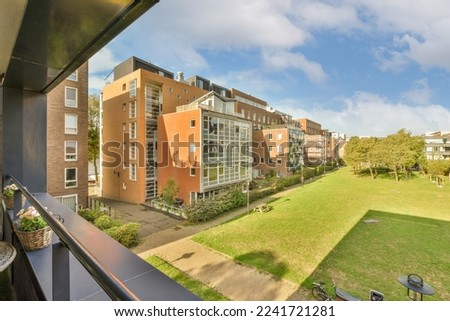 an outside area with some buildings and green grass in the photo is taken from a balcony looking out onto the street