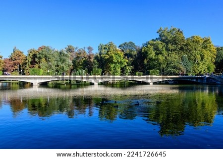 Landscape with long old grey bridge and many large green trees near the lake in Carol Park in Bucharest, Romania,  in a sunny autumn day