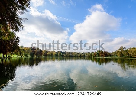 Landscape with many large green and yellow old trees near the lake in a sunny autumn day in Tineretului Park in Bucharest, Romania Royalty-Free Stock Photo #2241726649