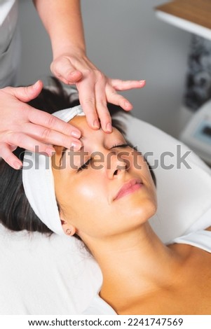 Beautiful young brunette with closed eyes enjoying facial massage at beauty spa center