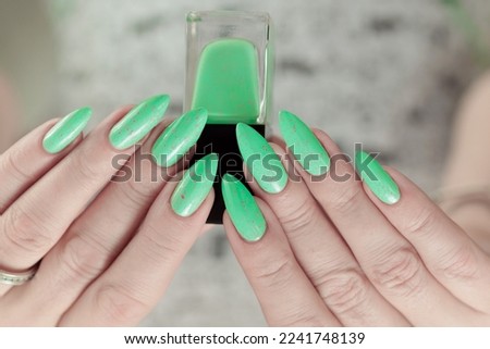 Female hand with long nails and neon light green manicure with bottles of nail polish