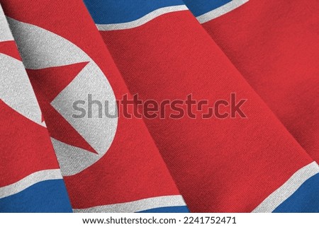 North Korea flag with big folds waving close up under the studio light indoors. The official symbols and colors in fabric banner