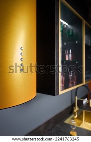 Contemporary cylinder golden range hood or extractor hood in kitchen for island cooker design, controls panel closeup view over out of focus kitchen cupboard and sink interior background.