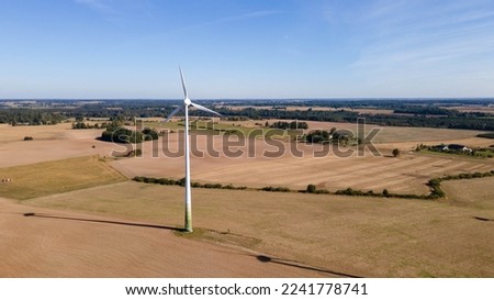 One wind turbine stands in a golden wheat field. Against the backdrop of a bright blue sky, and green trees and bushes. Photo from a bird's eye view, from a drone.