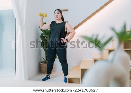 fat woman standing lifting dumbbell workout in living room. chubby woman raising arm using dumbbell building muscle. motivated overweight woman workout holding exercise tool lifting dumbbell up down. Royalty-Free Stock Photo #2241788629