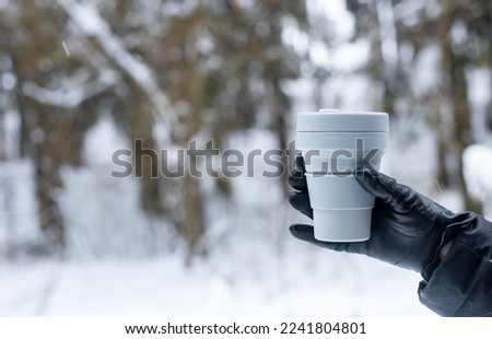 Hand in glove holding takeaway eco coffee cup, takeout tea mug on winter holidays, background for text. High quality photo