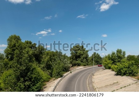 Top view of the asphalt road and a red car in the distance. Green big plants near the asphalt road. travel by car