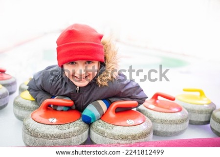 a little boy lies near the granite stones on the ice after a sport game of curling