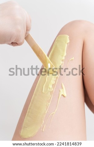Closeup hand in glove applying green hot wax on woman leg using spatula. Professional depilation procedure with hot wax in beauty salon. Part of photo series.