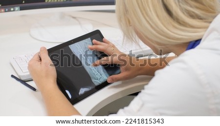 A blond veterinarian woman sits with her back to the camera and holds an ipad in her hands with an x-ray of an animal. The veterinarian will examine the x-rays of the dog.