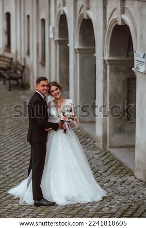 newlyweds in love on their wedding day pose for a photographer against the background of nature; he is in a dark classic jacket and she is in a white dress; a very happy and cheerful couple of people 