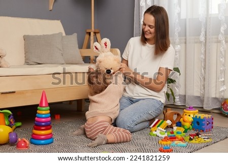 Portrait of happy mom and daughter playing, early education and development, loving family having fun together playing with plush soft toys at home on the floor.