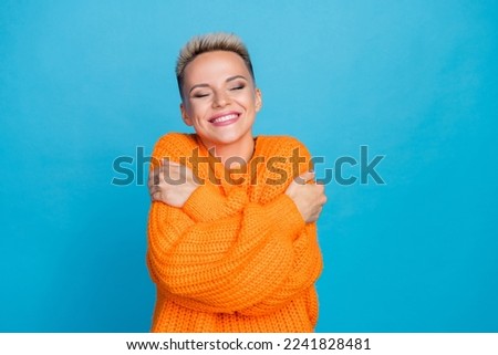 Photo portrait of pretty young girl cuddle self cheerful shiny smile dressed stylish orange clothes isolated on blue color background