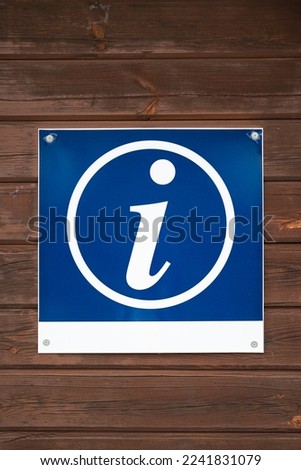 Blue sign with info icon hanging on brown lumber wall of cabin in daytime