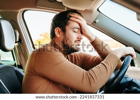 Side view young male driver closed his eyes and rests with his hand on the steering wheel and the other on his forehead. To work productively, you need to have a good rest. The guy is tired. Royalty-Free Stock Photo #2241837331