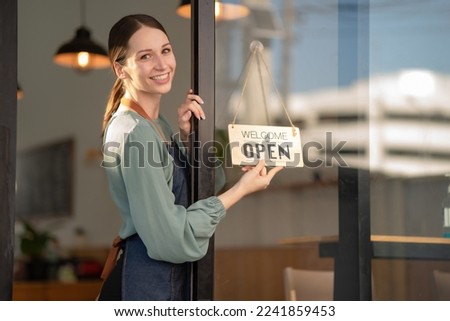 A beautiful young coffee shop owner holds an open sign.