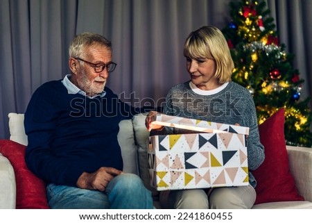 Romantic sweet senior couple having fun and smiling while celebrating enjoying opening magic christmas box.Senior man giving gift box surprise to wife in valentines day at home	