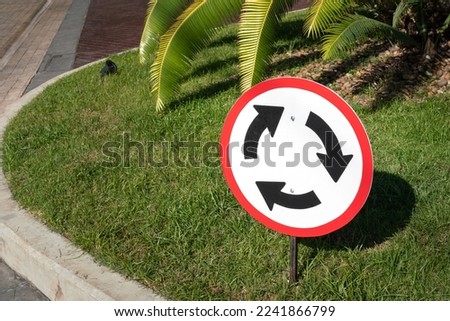A roundabout direction sign metal plate which is installed on grass ground. Road sign object photo, close-up and selective focus.