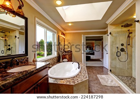 Luxury bathroom interior with skylight. Bath tub with mosaic trim and two wooden vanity cabinets