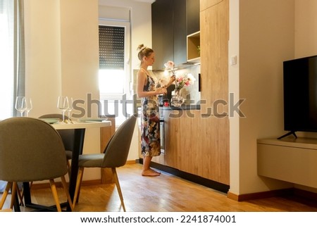 Woman arranging vase with flowers on the kitchen counter. Housewife taking care of coziness in apartment. Interior decor, household and home improvement concept. Royalty-Free Stock Photo #2241874001