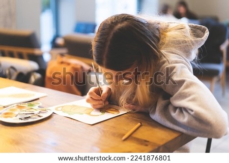Pretty teenage girl draws a picture with poster paint. Front view of a drawing of a girl with a palette in her hand. A smiling young teenage girl draws a picture