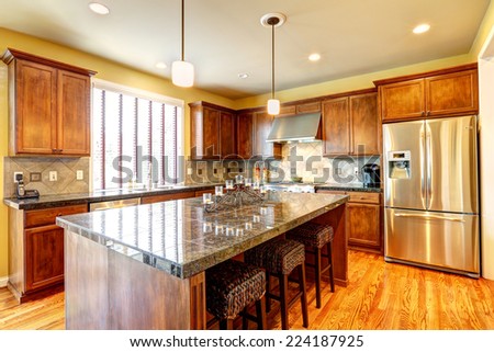Luxury kitchen room with modern storage combination and steel appliances. Big kitchen island with granite top and wicker stools