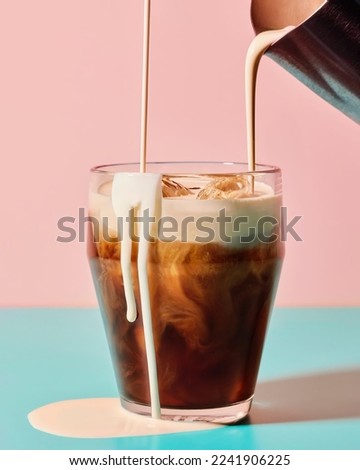 milk is poured into a glass of coffee until it overflows Royalty-Free Stock Photo #2241906225
