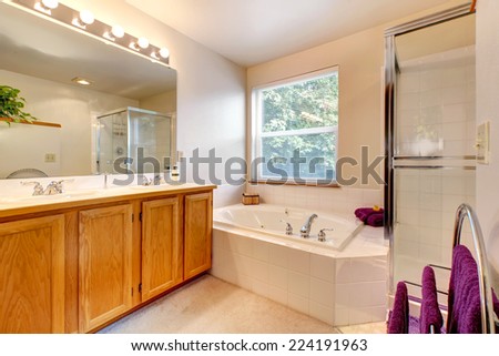 Bathroom vanity cabinet with mirror, bath tub with tile trim and glass door shower. Room decorated with purple towels