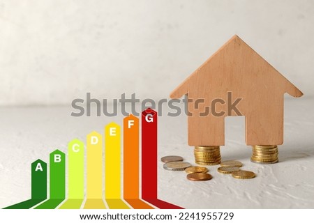 House figure with coins and energy efficiency rating on light background. Concept of smart home Royalty-Free Stock Photo #2241955729