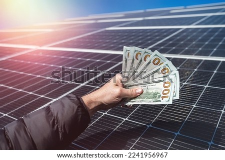 young wonderful worker is holding a round amount of money for the installation of solar panels in his hands. Concept of green electricity and dollars. saving electricity Royalty-Free Stock Photo #2241956967
