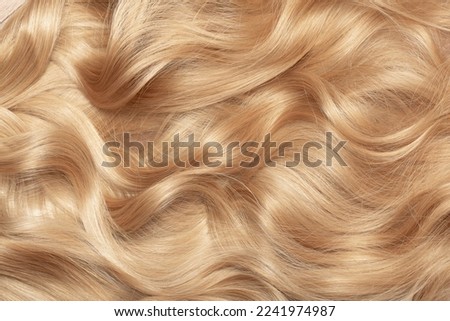 Blond hair close-up as a background. Women's long blonde hair. Beautifully styled wavy shiny curls. Hair coloring. Hairdressing procedures, extension. Royalty-Free Stock Photo #2241974987