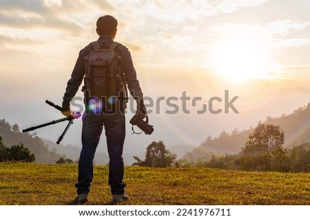 professional photographer with camera and tripod looking mountain sunset background