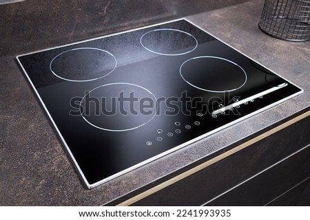 Grey countertop with black glossy built in ceramic glass induction or electric hob stove cooker with four burners in dark empty modern contemporary flat design loft kitchen interior. Royalty-Free Stock Photo #2241993935