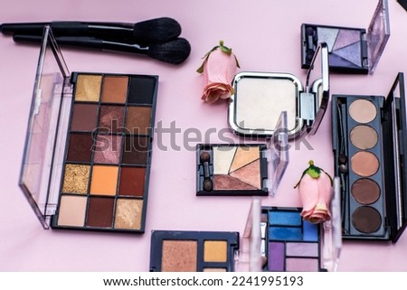 eyeshadows multicolored powder, two brushes, roses on pink background. Beauty product and make-up concept top view