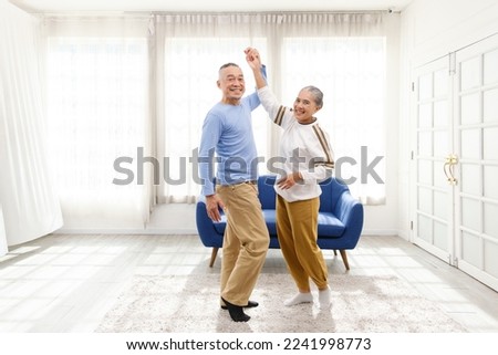 Romantic and cheerful Asian well-being senior couple enjoy dancing and holding hands to music together with smiles and happiness in the living room. Senior retirement activity at home. Royalty-Free Stock Photo #2241998773