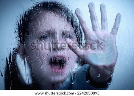 Young girl with a raised hand showing STOP gesture behind wet glass.