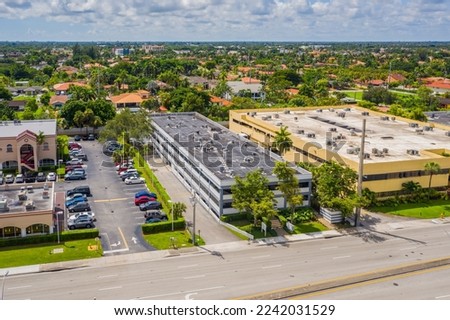 Facade of a gray and white office building, with two floors, with. parking lot, sidewalk, street, driveway with trees, short grass, blue sky, urban skyline