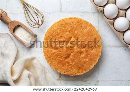 Just baked plain vanilla sponge cake on the cooking iron grid, white table, directly above. Fluffy, moist and rich chiffon Cake, two layers, homemade . Cooking utensils and ingredients on background. Royalty-Free Stock Photo #2242042969
