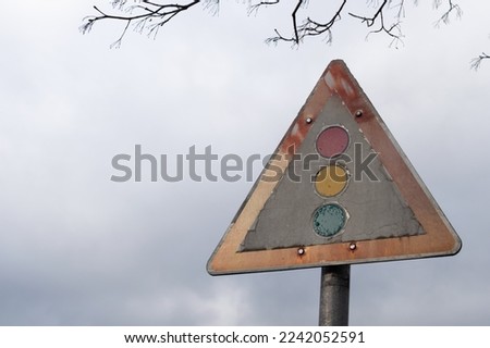 Warning traffic sign for a traffic light in worn out condition with a dramatic gray cloudy sky